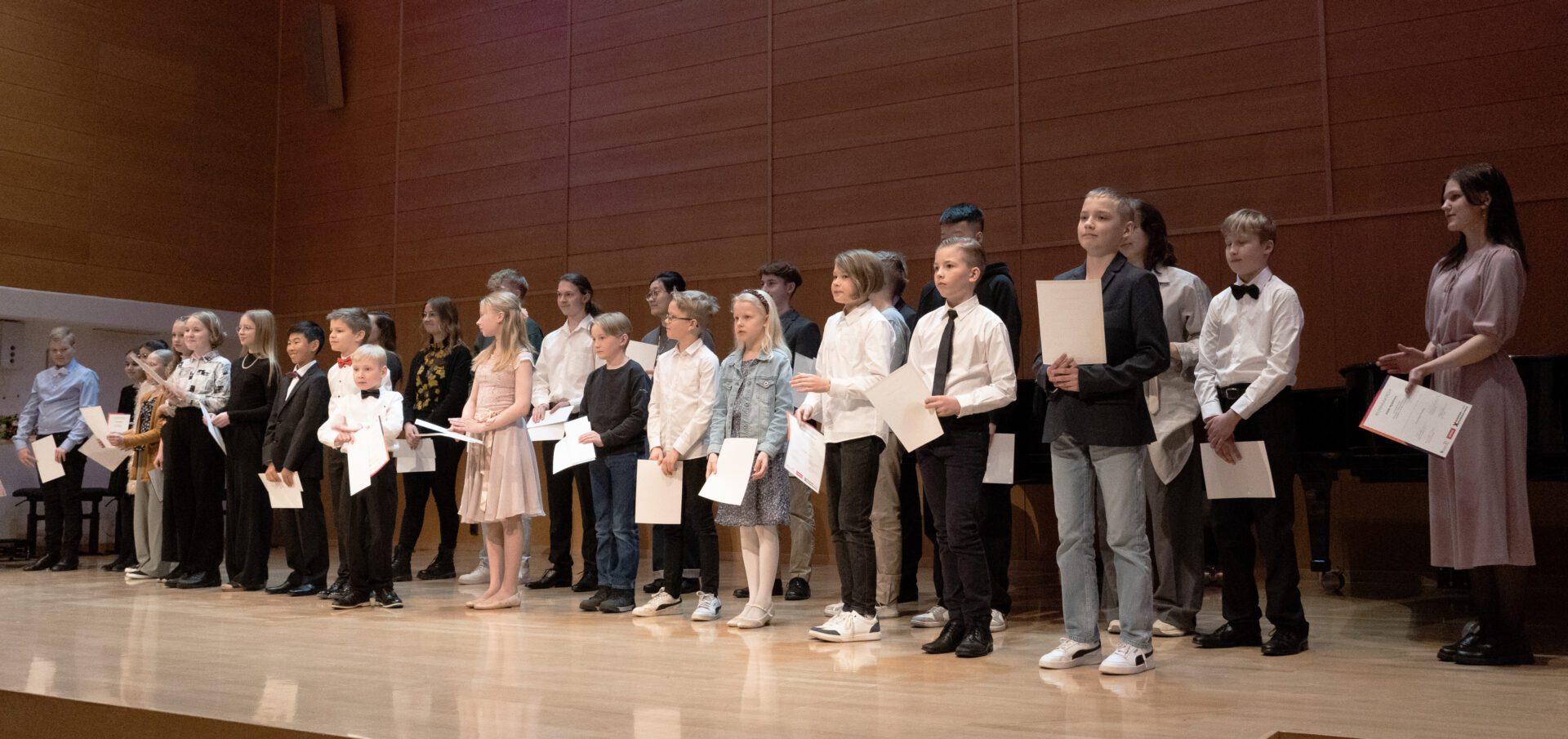 Pianokilpailun osallistujia Kamarimusiikkisalin lavalla kunniakirjat käsissään.